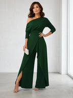 Driftly green asymmetrical one-shoulder jumpsuit with crossed detail and flowing wide-leg trousers, in a minimalist studio setting with soft window light.
