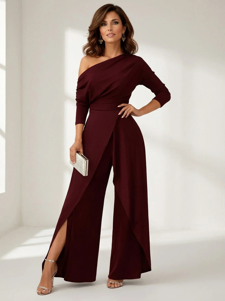 Driftly red asymmetrical one-shoulder jumpsuit with crossed detail and flowing wide-leg trousers, in a minimalist studio setting with soft window light.