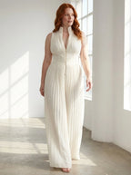 Woman wearing a white pleated sleeveless jumpsuit in a bright minimalist interior