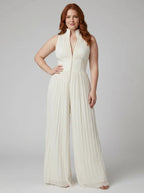 Woman wearing a white pleated sleeveless jumpsuit with structured collar and front zip, studio shot