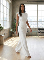Woman wearing a white sculptural straight-leg jumpsuit indoors in a bright loft interior
