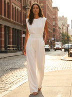 Woman wearing a white sculptural straight-leg jumpsuit on a sunlit city street