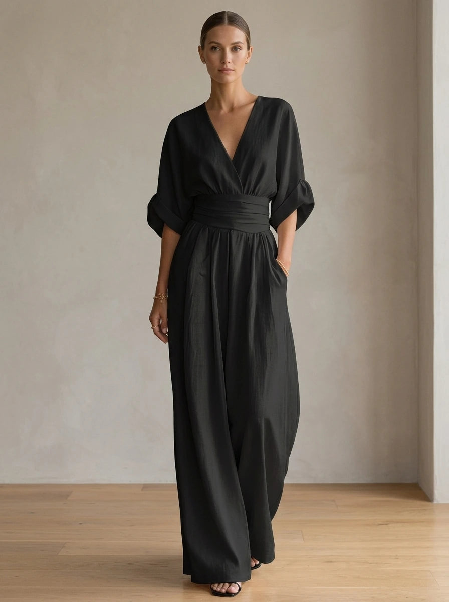 Driftly black deep V-neck jumpsuit with relaxed short sleeves, ruched waist, and fluid wide-leg trousers, in a minimalist studio setting with soft window light.