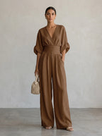 Driftly brown deep V-neck jumpsuit with relaxed short sleeves, ruched waist, and fluid wide-leg trousers, in a minimalist studio setting with soft window light.