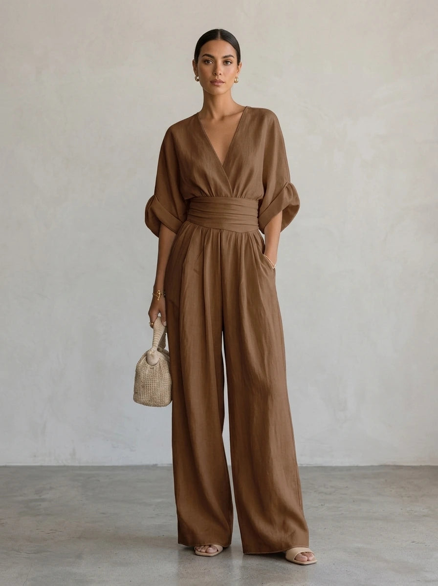 Driftly brown deep V-neck jumpsuit with relaxed short sleeves, ruched waist, and fluid wide-leg trousers, in a minimalist studio setting with soft window light.