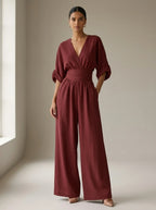Driftly burgundy deep V-neck jumpsuit with relaxed short sleeves, ruched waist, and fluid wide-leg trousers, in a minimalist studio setting with soft window light.