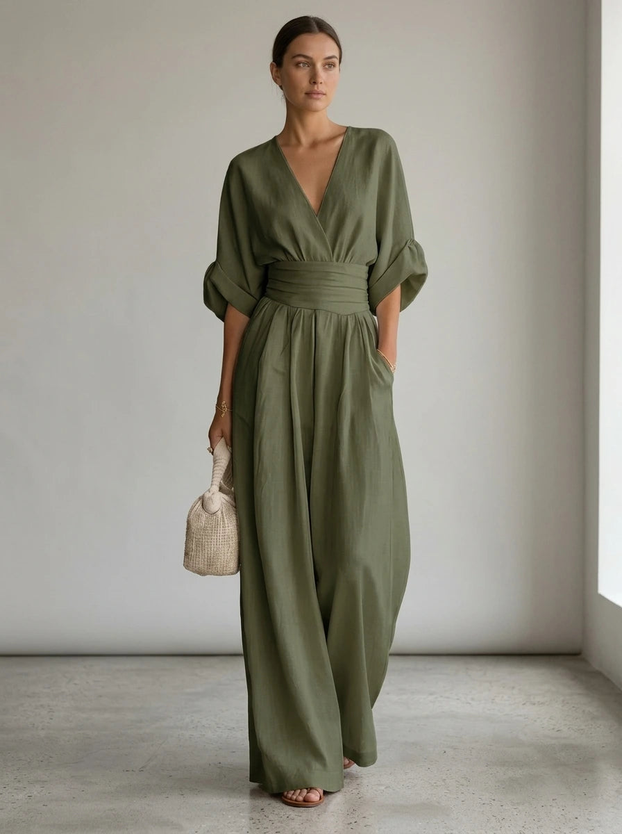 Driftly green deep V-neck jumpsuit with relaxed short sleeves, ruched waist, and fluid wide-leg trousers, in a minimalist studio setting with soft window light.