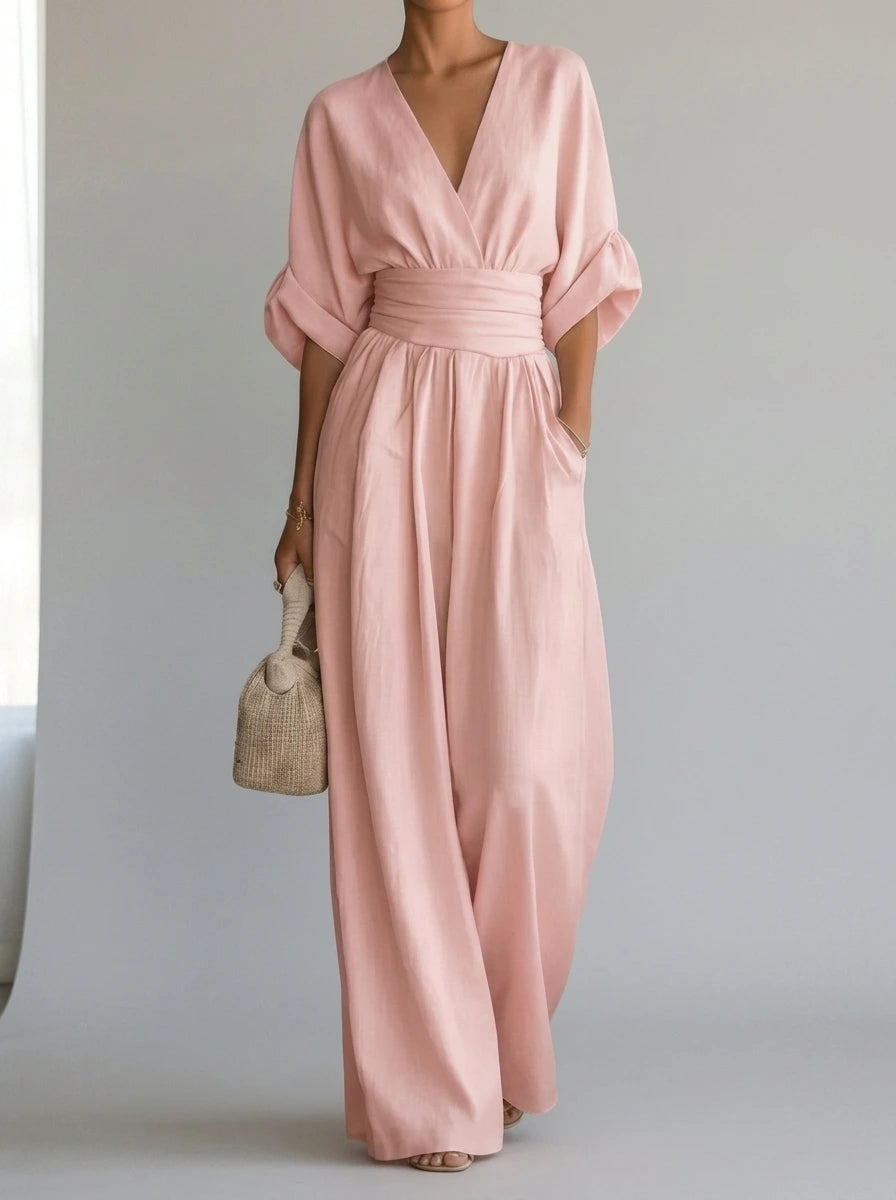 Driftly light pink deep V-neck jumpsuit with relaxed short sleeves, ruched waist, and fluid wide-leg trousers, in a minimalist studio setting with soft window light.