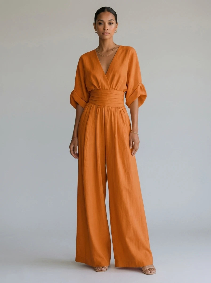 Driftly orange deep V-neck jumpsuit with relaxed short sleeves, ruched waist, and fluid wide-leg trousers, in a minimalist studio setting with soft window light.
