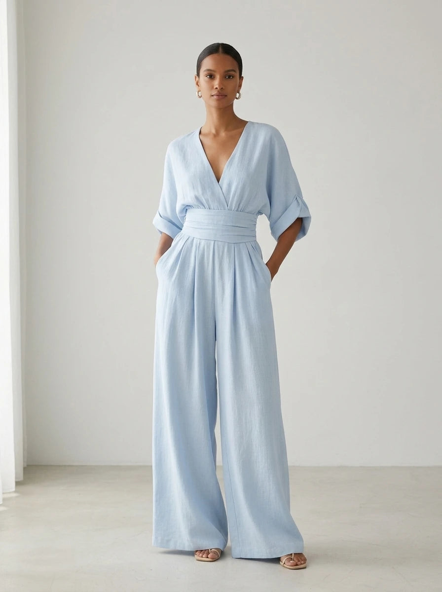 Driftly sky blue deep V-neck jumpsuit with relaxed short sleeves, ruched waist, and fluid wide-leg trousers, in a minimalist studio setting with soft window light.
