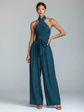 Woman wearing a teal blue wide-leg halter jumpsuit with tie waist, studio shot