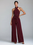 Woman wearing a burgundy red wide-leg halter jumpsuit with tie waist, studio shot
