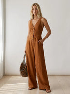 Driftly brown V-neck wide-leg jumpsuit with front button closure and side pockets, linen-effect fabric, in a minimalist studio setting with soft window light.