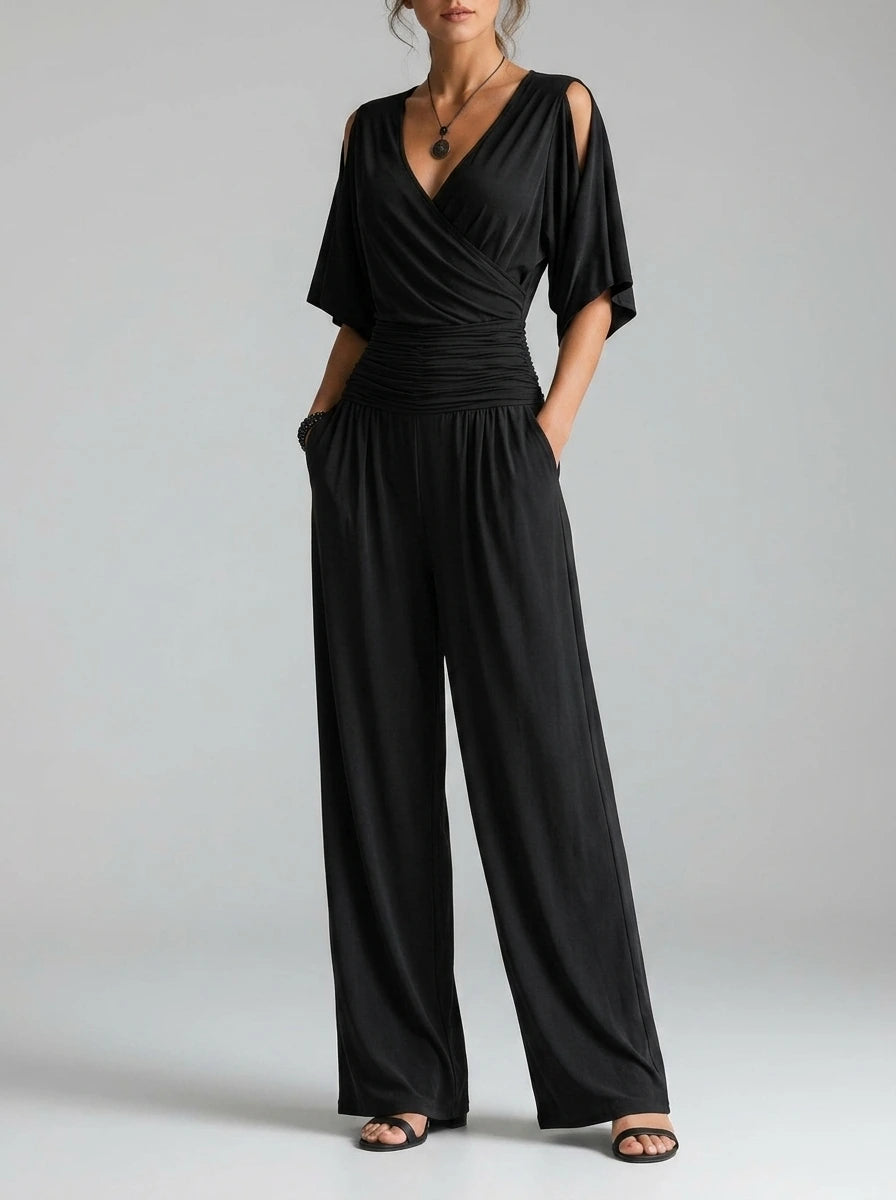 Driftly black crossed V-neck wrap jumpsuit with kimono style wide sleeves and a ruched waist, in a minimalist studio setting with soft window light.
