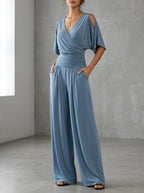 Driftly blue crossed V-neck wrap jumpsuit with kimono style wide sleeves and a ruched waist, in a minimalist studio setting with soft window light.
