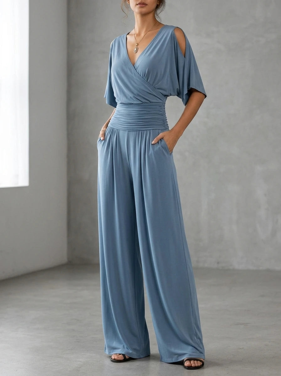 Driftly blue crossed V-neck wrap jumpsuit with kimono style wide sleeves and a ruched waist, in a minimalist studio setting with soft window light.