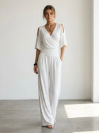 Driftly white crossed V-neck wrap jumpsuit with kimono style wide sleeves and a ruched waist, in a minimalist studio setting with soft window light.