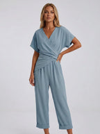Woman wearing a blue wrap V-neck jumpsuit with draped waist, studio shot