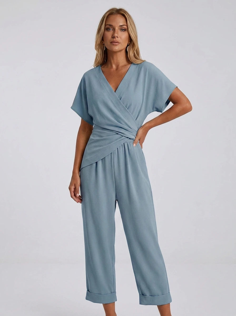 Woman wearing a blue wrap V-neck jumpsuit with draped waist, studio shot