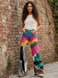 Woman wearing multicolor boho chic flared pants against a brick wall
