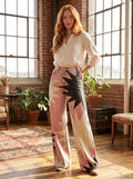Woman wearing pink bohemian chic high-waisted patterned pants, standing in a sunlit loft