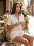 Woman wearing a white linen short sleeve shirt and shorts set, seated at a cafe terrace