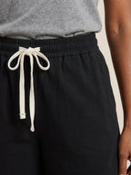 Close-up of black cotton wide-leg shorts showing elastic waistband and white drawstring.