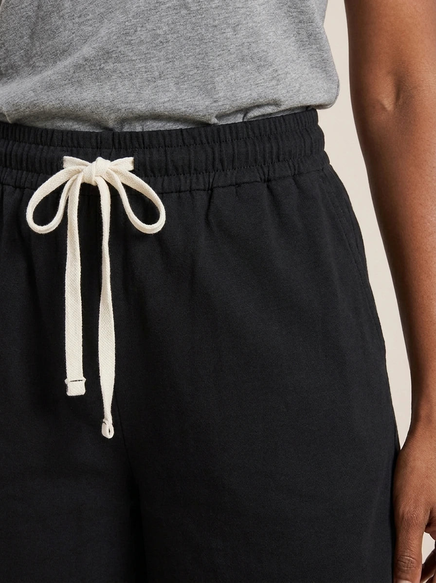 Close-up of black cotton wide-leg shorts showing elastic waistband and white drawstring.