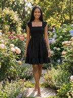 Driftly women's black smocked square-neck sundress, walking through a lush garden