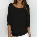 Woman wearing a black relaxed knit sweater with wide neckline and dolman sleeves, studio shot