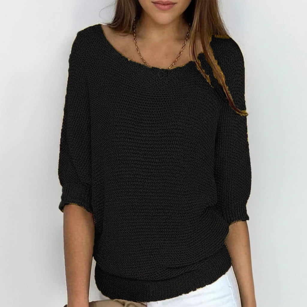 Woman wearing a black relaxed knit sweater with wide neckline and dolman sleeves, studio shot