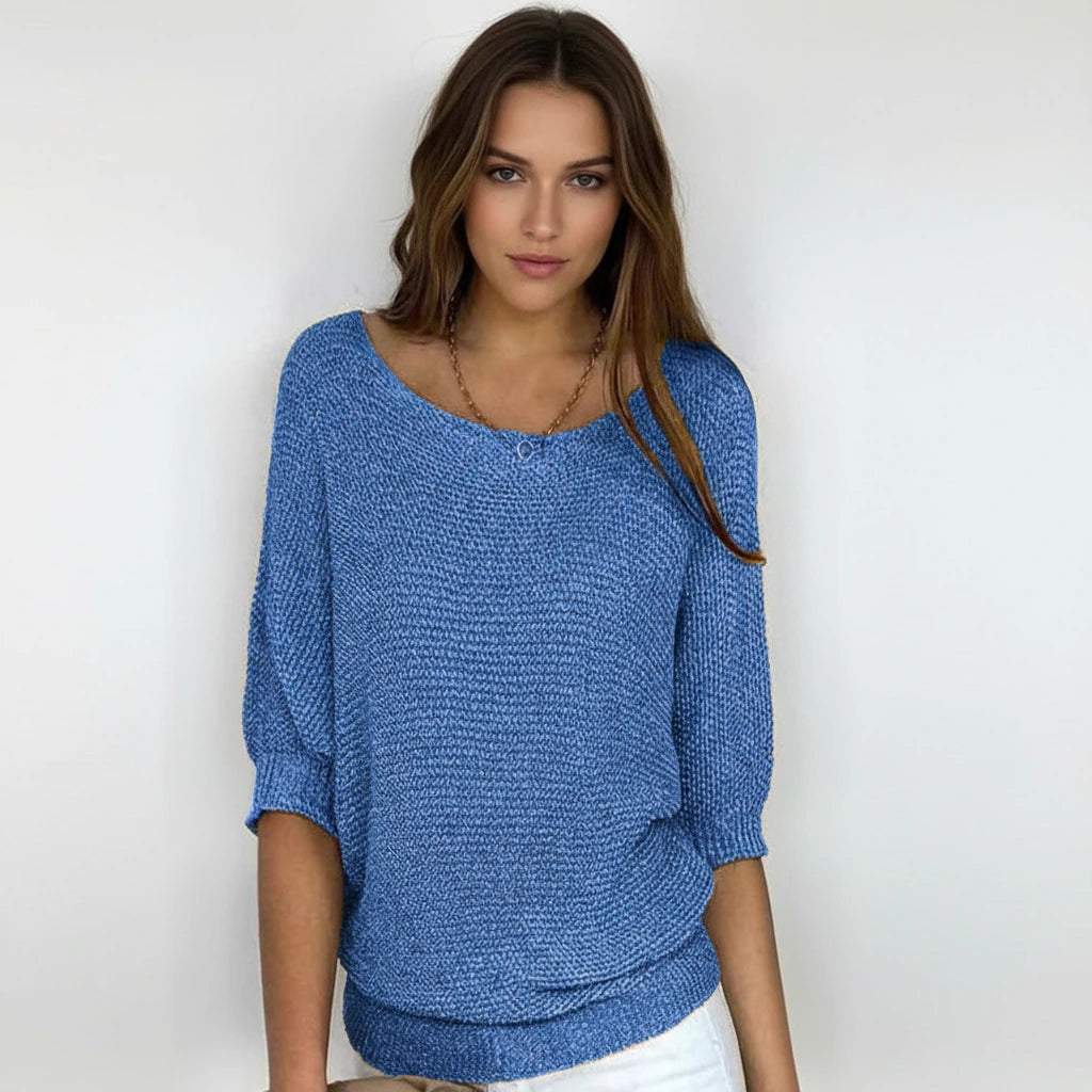 Woman wearing a blue relaxed knit sweater with wide neckline and dolman sleeves, studio shot