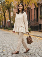 Cream cable knit sweater with layered hem on model, outdoor autumn street