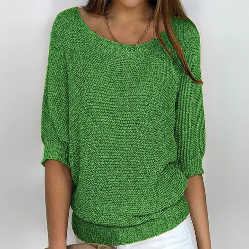 Woman wearing a green relaxed knit sweater with wide neckline and dolman sleeves, studio shot