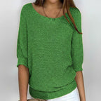 Woman wearing a green relaxed knit sweater with wide neckline and dolman sleeves, studio shot