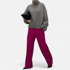 Woman wearing a grey oversized wool turtleneck sweater with magenta trousers in a lifestyle setting