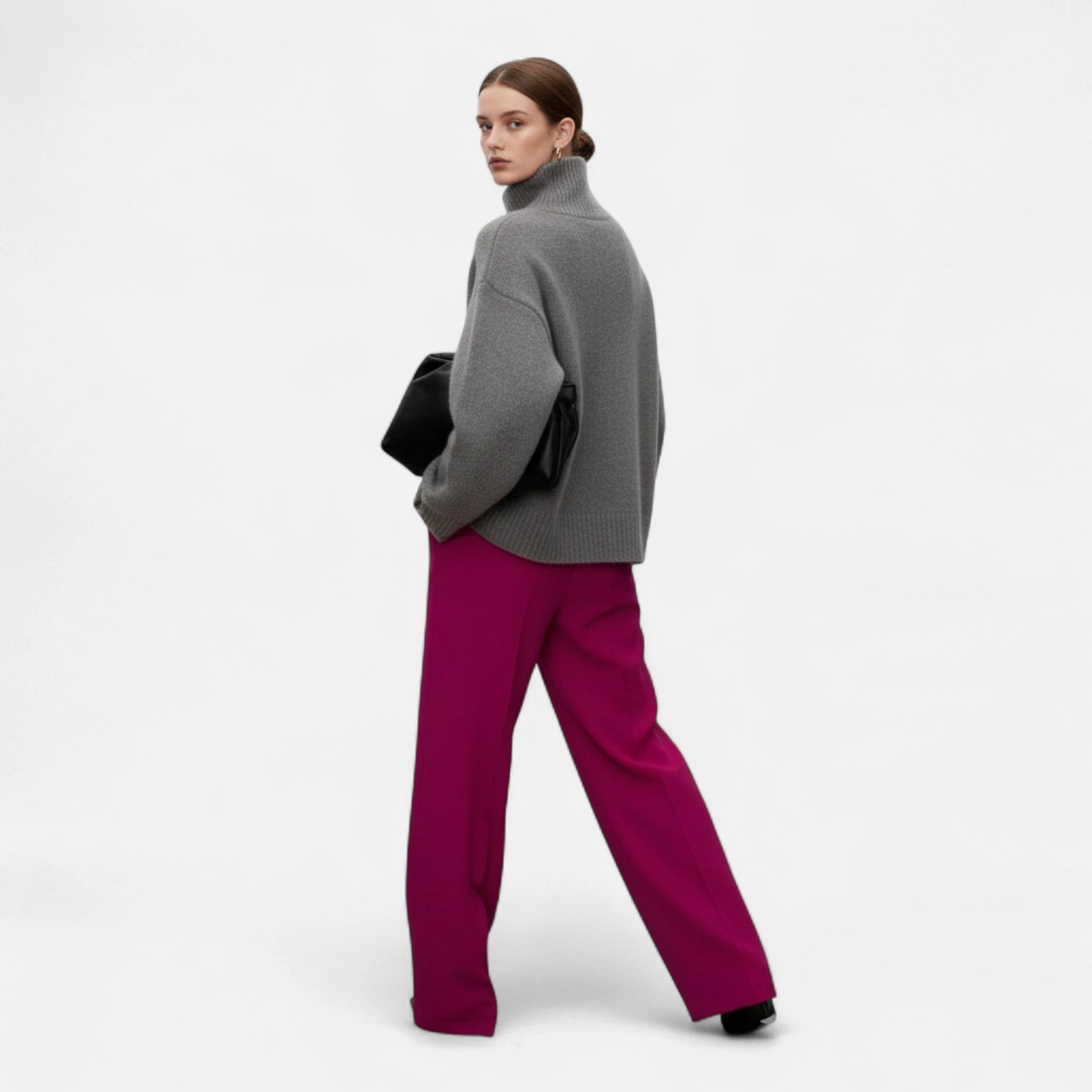 Woman wearing a grey oversized wool turtleneck sweater and carrying a black clutch, walking outdoors