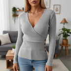 Woman wearing grey ribbed wrap sweater with side button detail in a living room