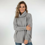 Woman wearing grey ribbed cowl neck sweater with button cuffs, studio photo