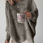 Woman wearing a grey oversized open knit sweater with draped asymmetric hem, studio shot