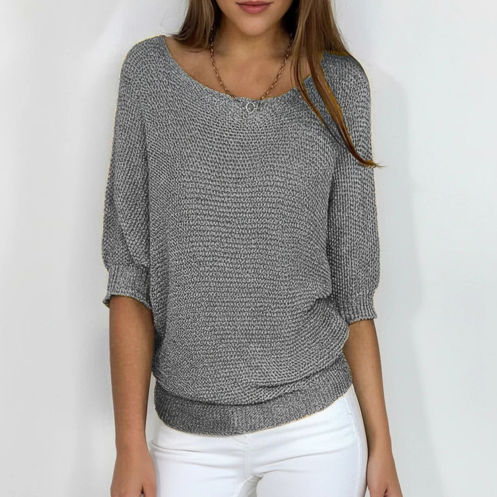 Woman wearing a grey relaxed knit sweater with wide neckline and dolman sleeves, studio shot