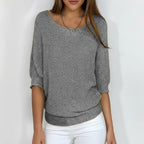 Woman wearing a grey relaxed knit sweater with wide neckline and dolman sleeves, studio shot