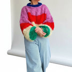 Woman wearing a hot pink striped chunky knit sweater with balloon sleeves, studio shot