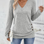 Woman wearing light grey V-neck sweater with side button detail, studio photo