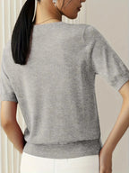 Woman wearing a light grey fine knit sweater with short sleeves, side view