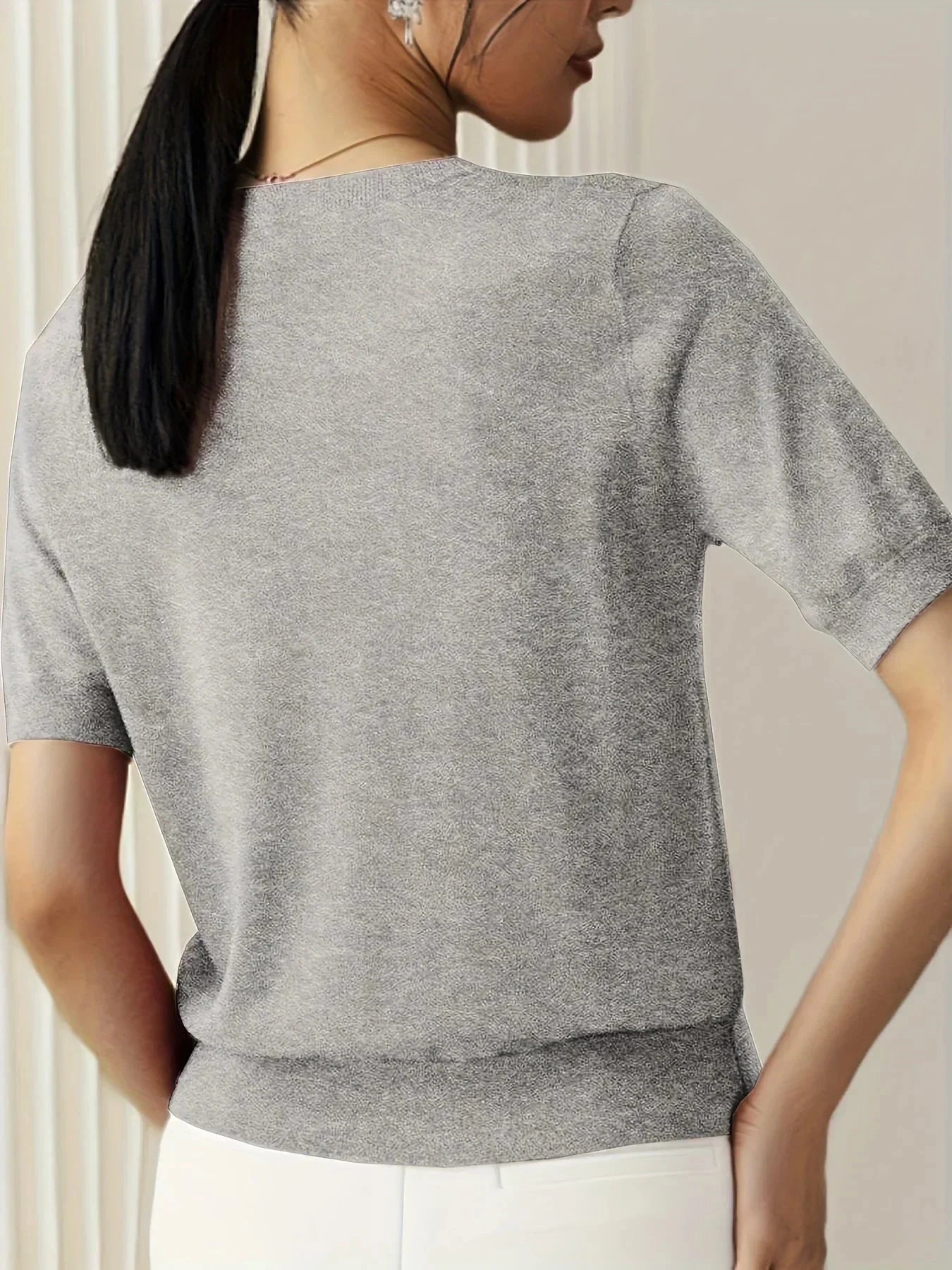 Woman wearing a light grey fine knit sweater with short sleeves, side view