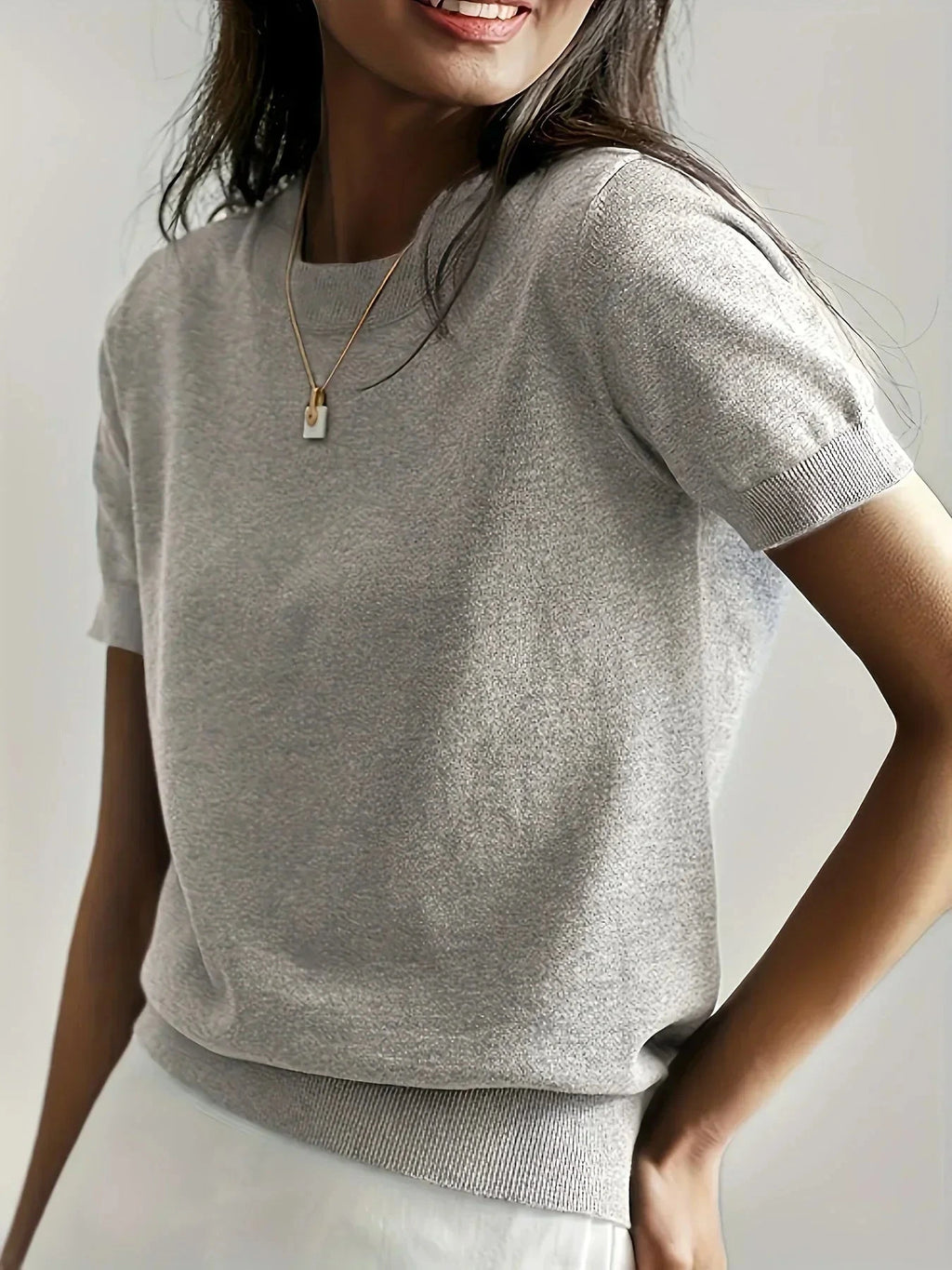 Woman wearing a light grey fine knit sweater with short sleeves and ribbed trim
