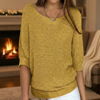Woman wearing a mustard yellow relaxed knit sweater by a fireplace, lifestyle shot
