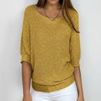 Woman wearing a mustard yellow relaxed knit sweater with wide neckline and dolman sleeves, studio shot