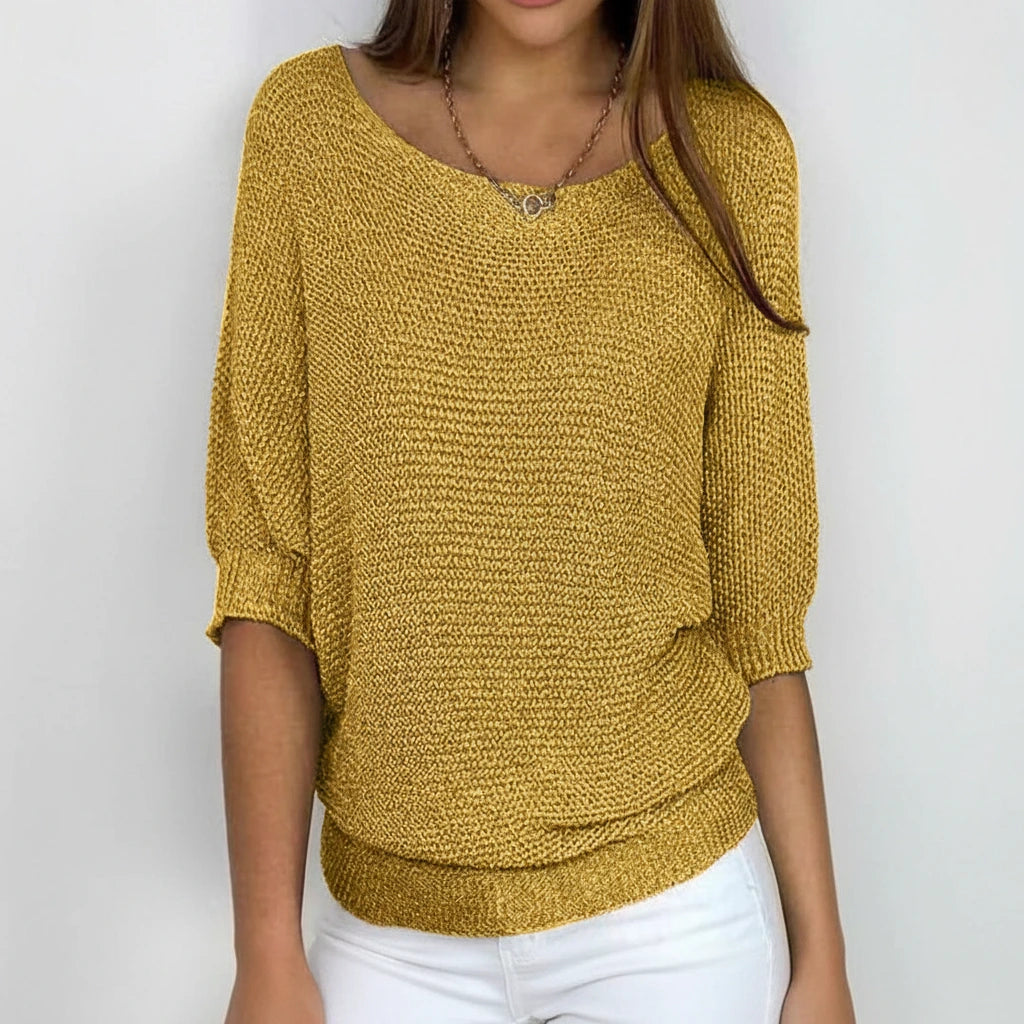 Woman wearing a mustard yellow relaxed knit sweater with wide neckline and dolman sleeves, studio shot